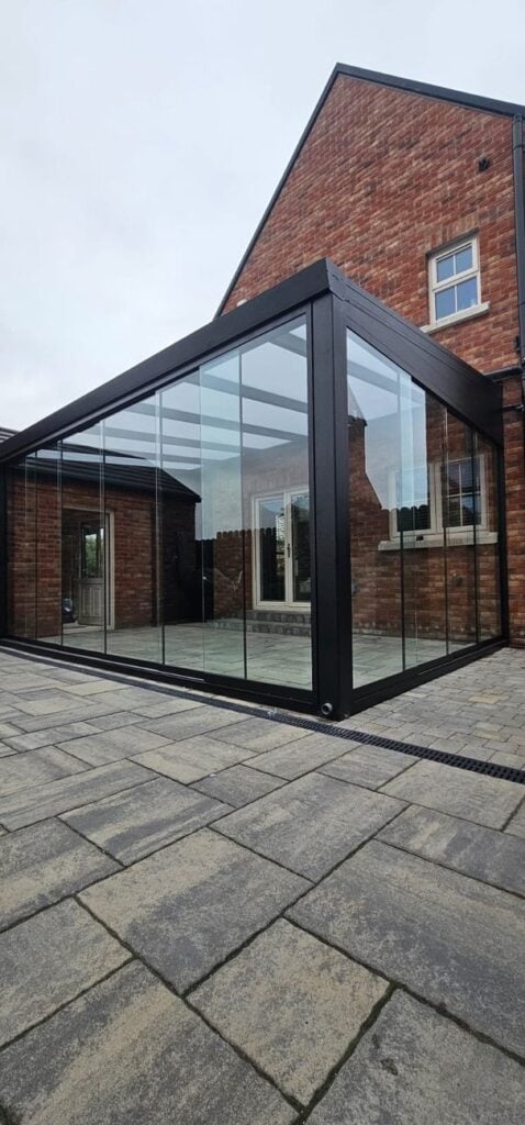 Black aluminium glass room with frameless sliding doors against a brick house