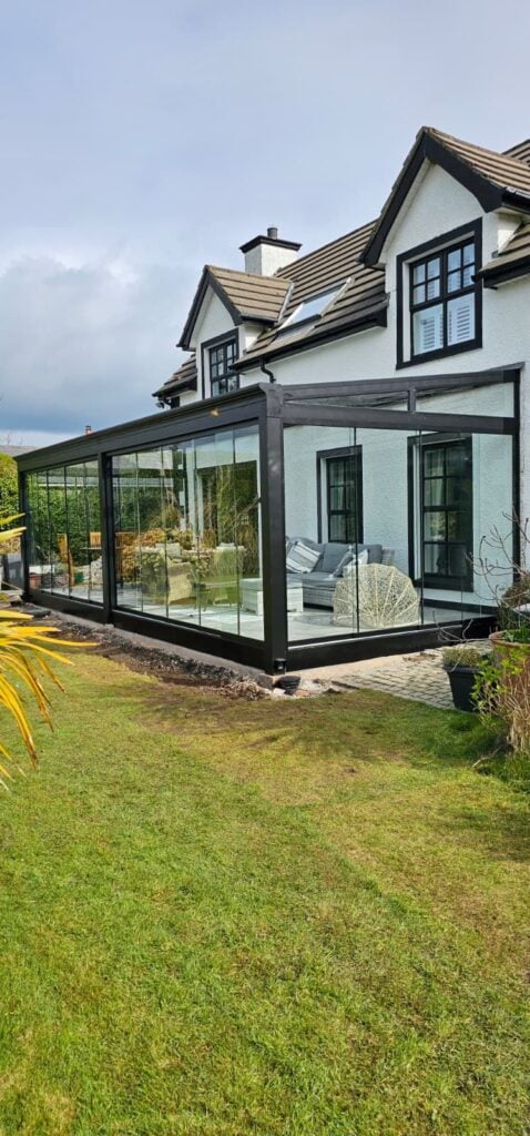 Glass room with a black frame on a cottage, seen from the lawn