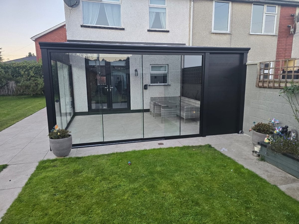 Glass room over a patio in Dundalk with frameless glass sliding doors and a solid aluminium wall on the neighbour's side