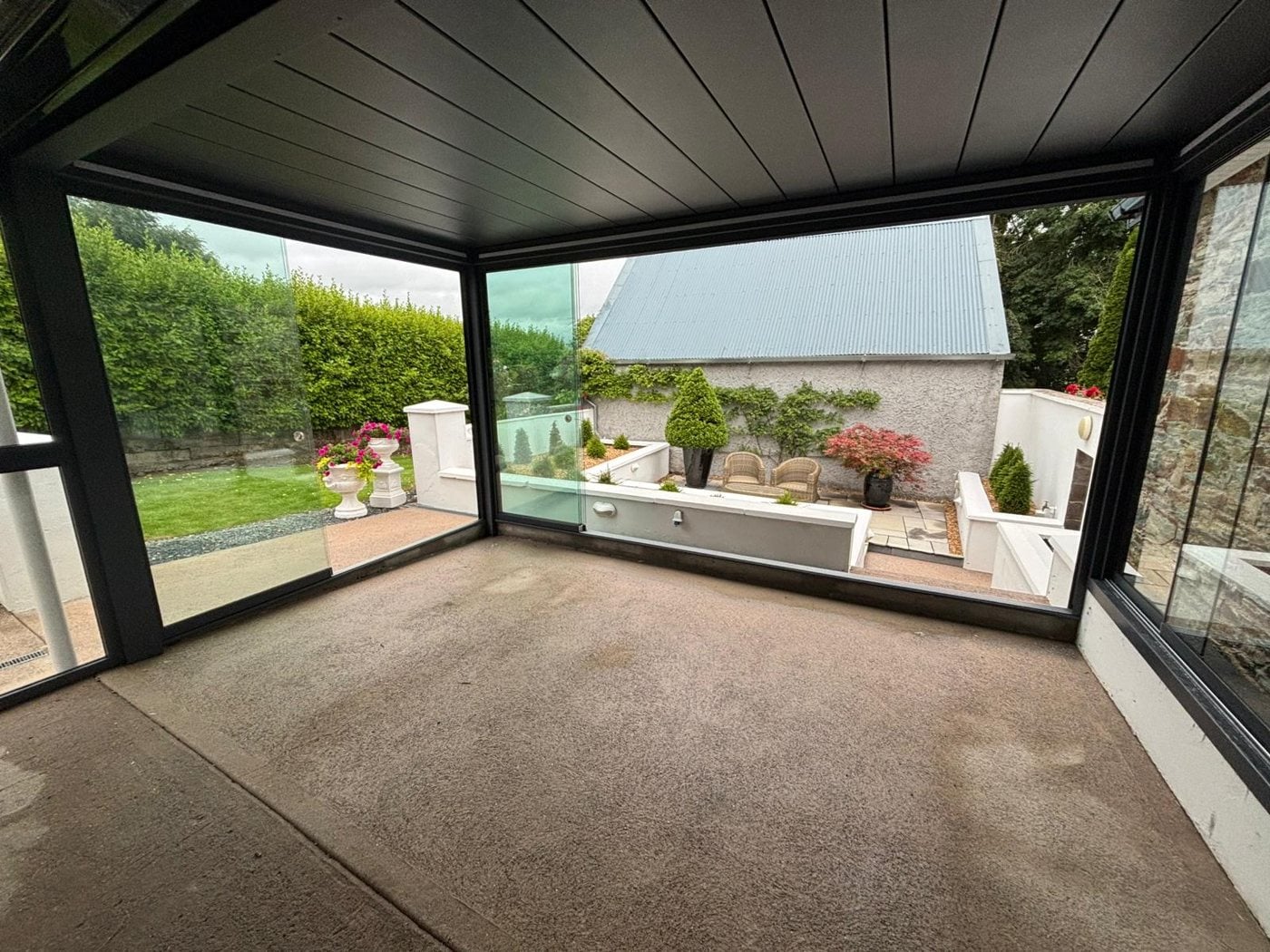 Inside a glass room under a closed aluminium roof, looking out to the garden
